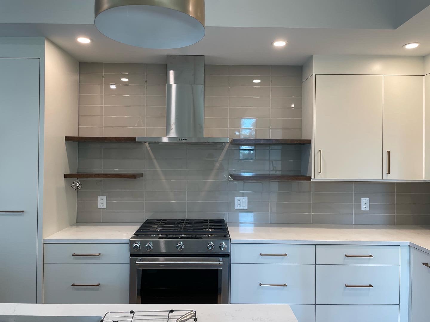 White slab kitchen with grey gloss subway backsplash and walnut floating shelves flanking a stainless hood